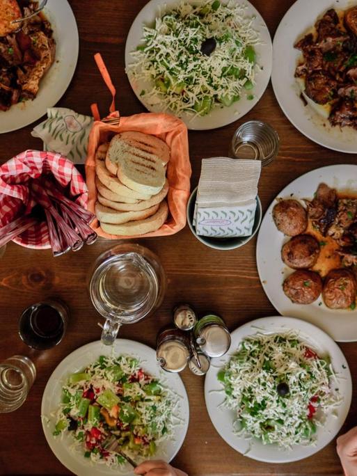 Eine gemütliche Dinner-Runde aus der Vogelperspektive. Auf einem Holztisch stehen zahlreiche Teller mit verschiedenen Speisen.