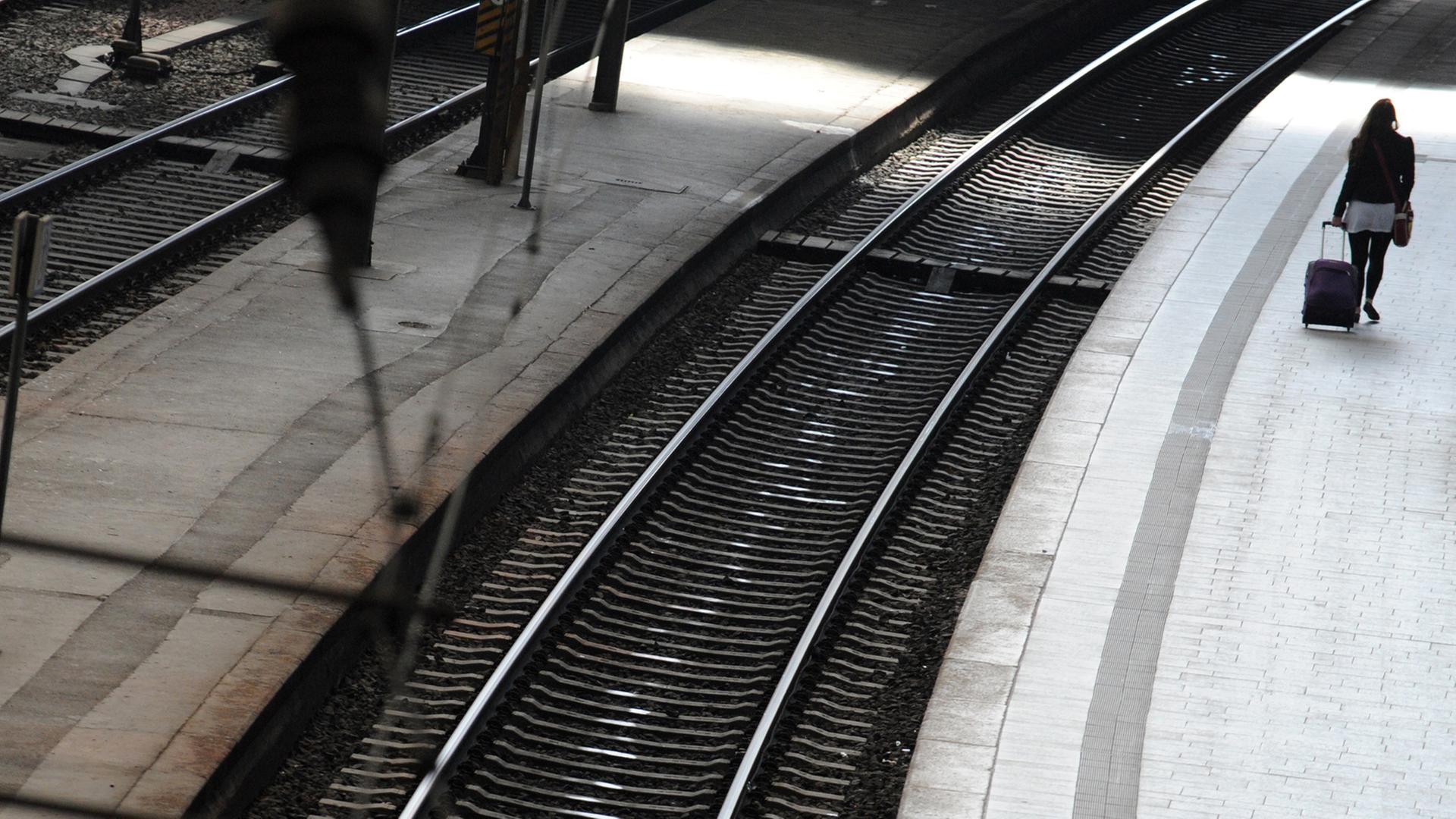 Eine Frau mit Roll-Koffer geht an einem leerem Bahn-Steig entlang