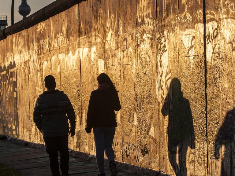 Eine Frau und ein Mann gehen am 18.04.2015 in Berlin im Licht der untergehenden Sonne an der East Side Gallery spazieren.
