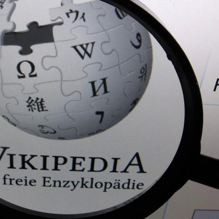 Auf einem Computerbildschirm ist das Logo der deutschen Version der freien Enzyklopädie Wikipedia durch eine Lupe vergrößert auf einem Computerbildschirm zu sehen. 