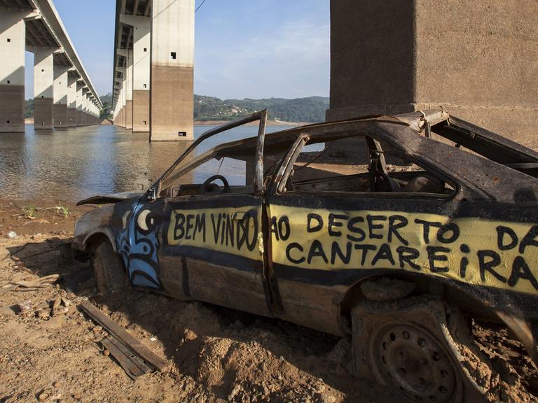 Brückenpfeiler und ein altes Autowrack sind an einem Fluss in Sao Paulo Brasilien zu sehen. Der Fluss führt ungewöhnlich wenig Wasser.