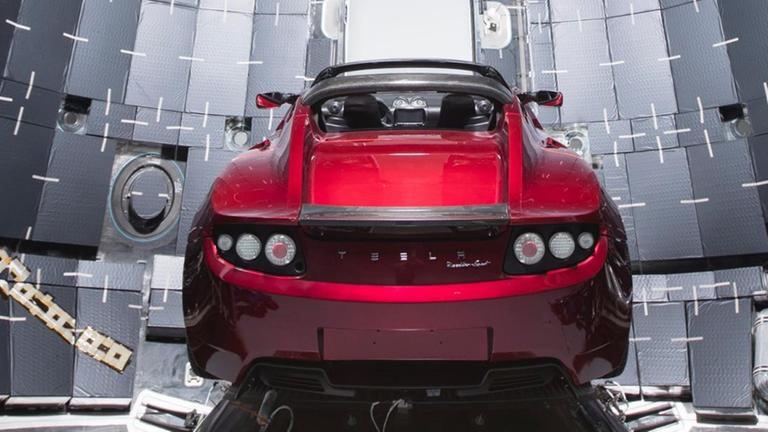Ein kirschroter Tesla Roadster wird im Inneren einer grauen Space X Rakete präsentiert.