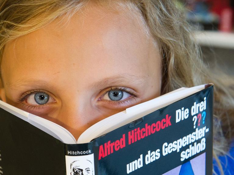 Ein Kind mit einem Buch aus der Reihe "Die drei ???"