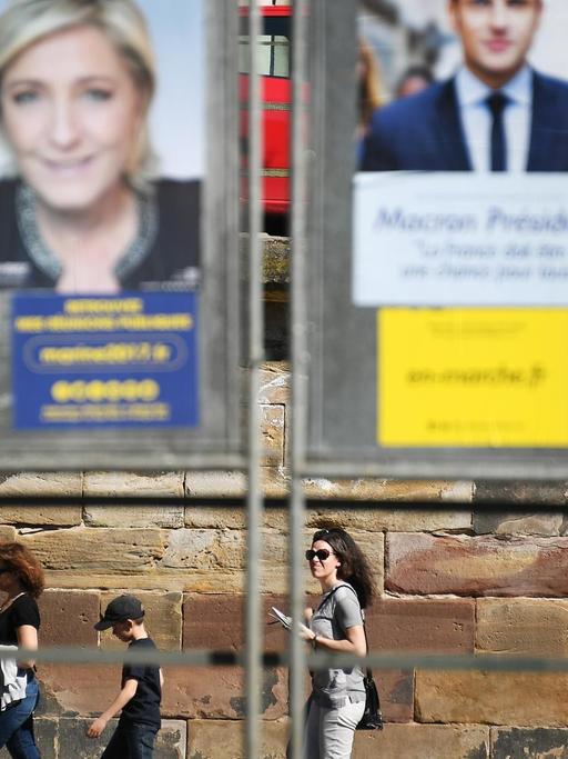 3 junge Leute spazieren unterhalb einer riesigen Plakatwand mit den Kandidaten der französischen Präsidentschaftswahlen am 10.04.2017, in Straßburg.