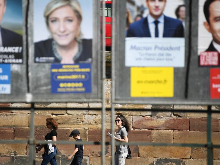 3 junge Leute spazieren unterhalb einer riesigen Plakatwand mit den Kandidaten der französischen Präsidentschaftswahlen am 10.04.2017, in Straßburg.