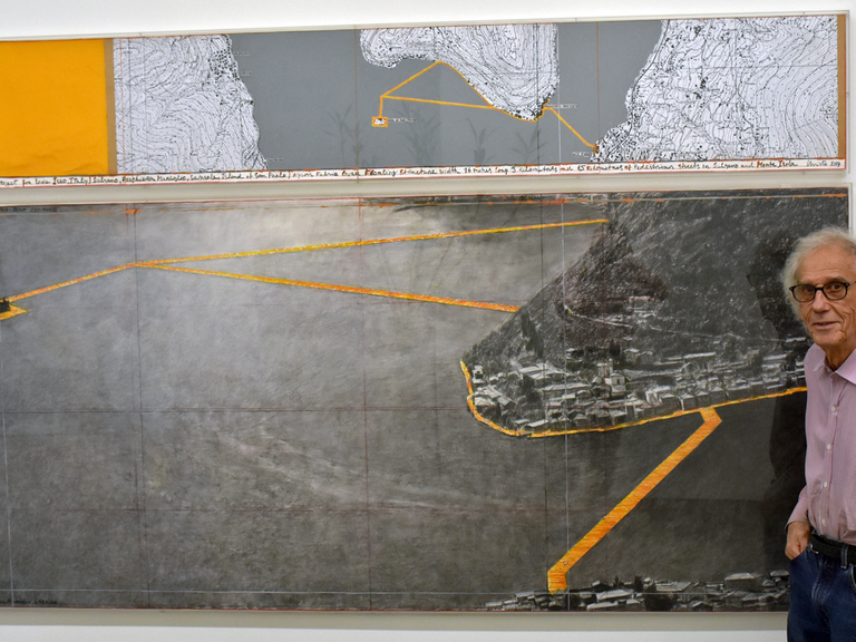 Christo in seinem Atelier in New York: Er steht vor einem Bild, das sein Projekt "Floating Piers" zeigt. Der Künstler möchte einen Steg aus knallgelben Kanistern bauen, der über den italienischen Iseo-See führt.