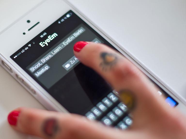 Eine Frau lädt während mit ihrem Smartphone ein Foto hoch.