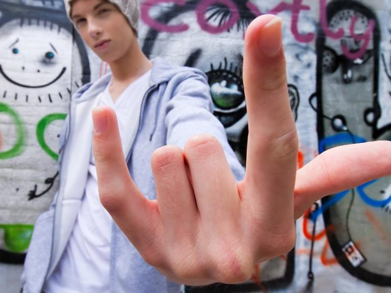 Ein cool blickender Jugendlicher posiert vor einer Wand mit Graffiti.