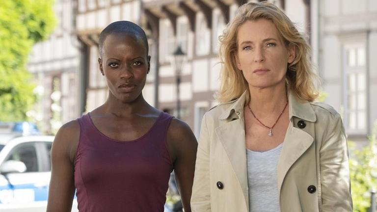 Florence Kasumba steht neben Maria Furtwängler. Beide stehen vor dem "Tatort"-Logo.