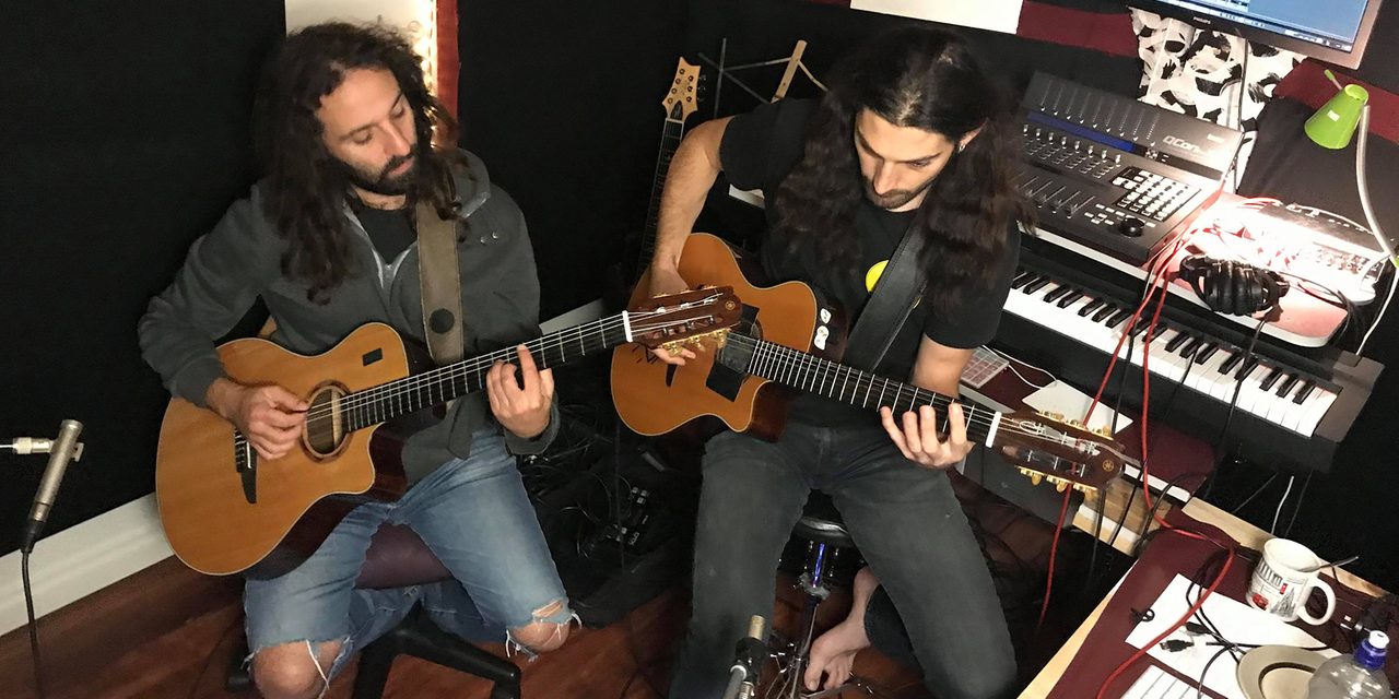 Zwei Männer mit langen schwarzen Haaren sitzen mit Akustik-Gitarren auf dem Schoß in einem Tonstudio. Zwei Männer mit langen schwarzen Haaren sitzen mit Akustik-Gitarren auf dem Schoß in einem Tonstudio.