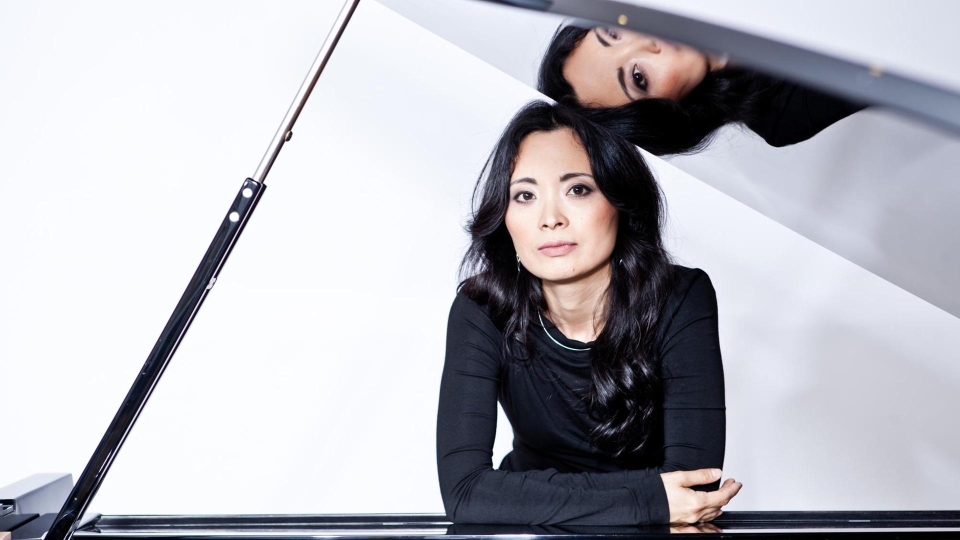 Ein Portrait der Pianistin Rei Nakamura am Flügel, deren Gesicht sich im Instrumentendeckel spiegelt