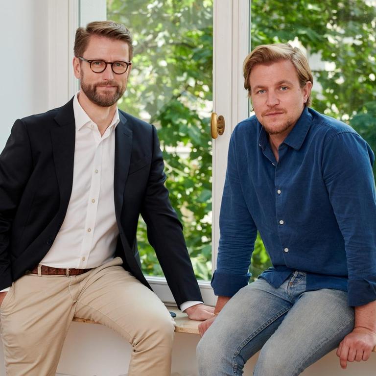 Die zwei Geschäftsführer von Aurora Europe Axel Gille und Philip Schetter stehen vor einem Fenster