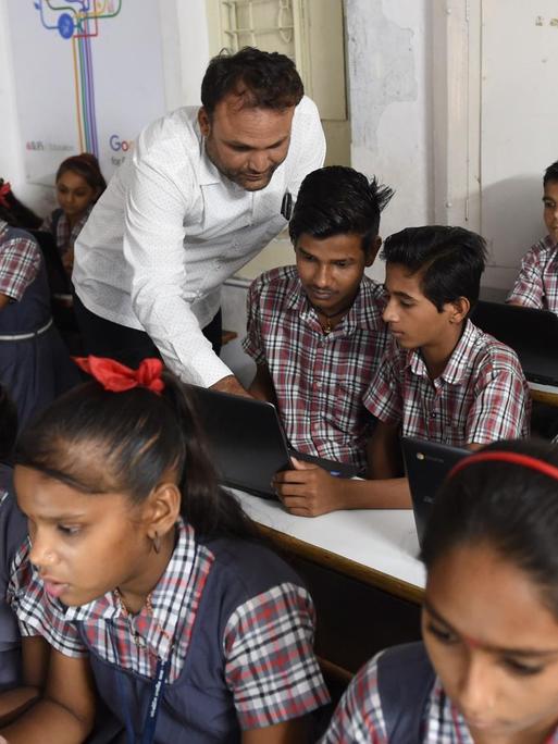 Das Foto zeigt eine öffentliche Schule in Ahmedabad/Indien im Juli 2018. Ein Lehrer erläutert den Schülerinnen und Schülern die Computer-Arbeit im E-Klassenraum.