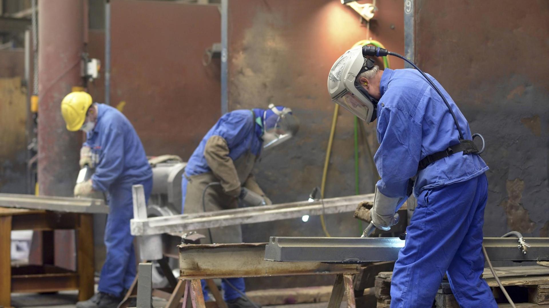 Drei Männer in Schutz-Kleidung arbeiten an Eisen-Teilen.