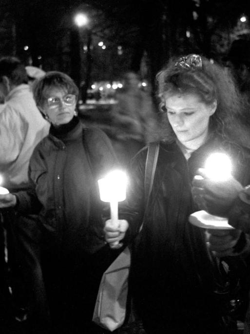 Eine historische schwarz/weiss Aufnahme von der letzten Montagsdemo in Leipzig 1989. Die Menschen stehen mit Kerzen in den Händen in einer Gruppe zusammen.