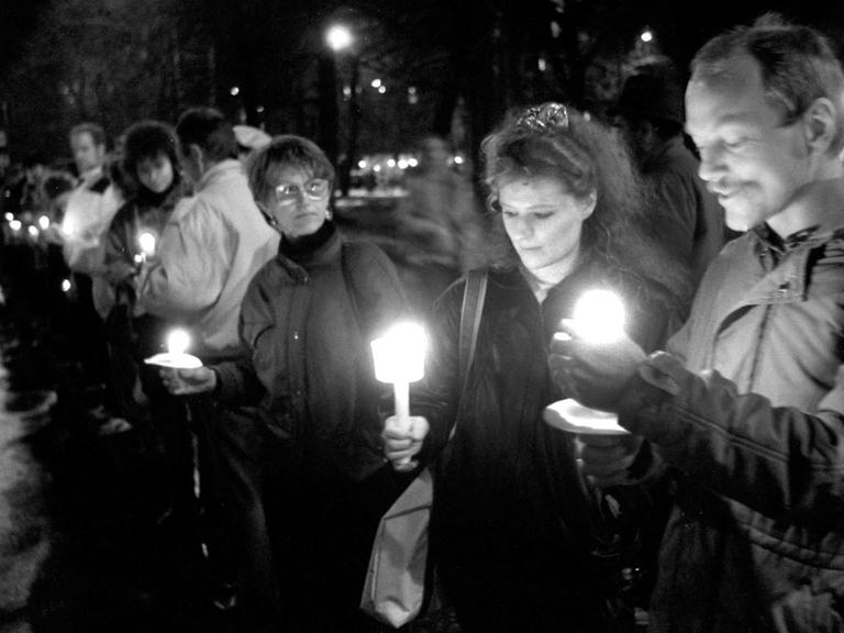 Eine historische schwarz/weiss Aufnahme von der letzten Montagsdemo in Leipzig 1989. Die Menschen stehen mit Kerzen in den Händen in einer Gruppe zusammen.