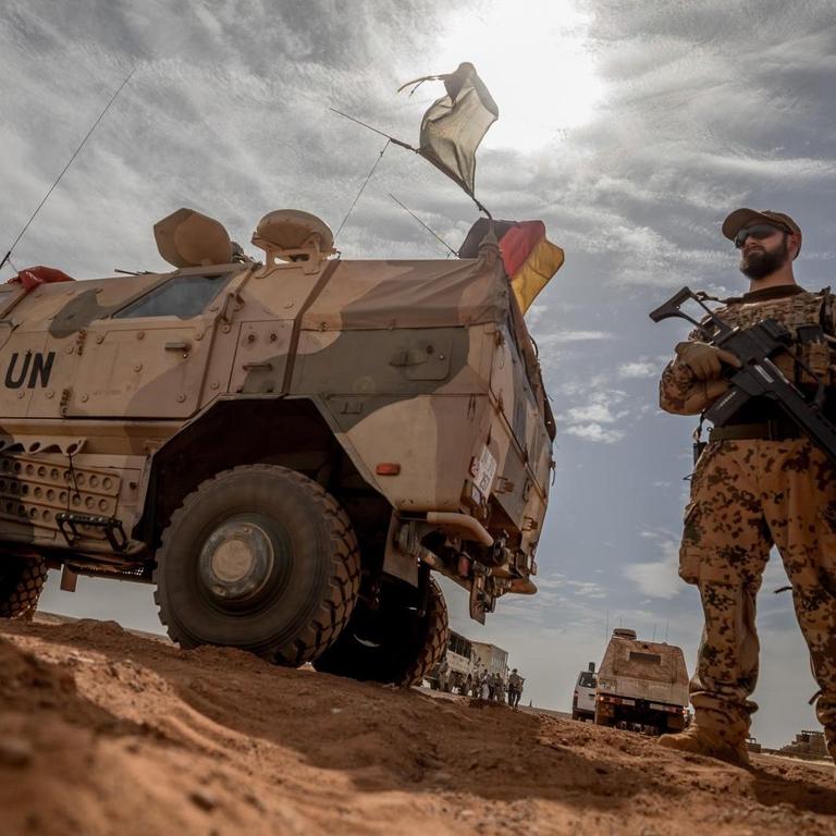 in Soldat der Bundeswehr steht neben einem Militärfahrzeug der UN, die deutsche Fahne weht hinter ihm