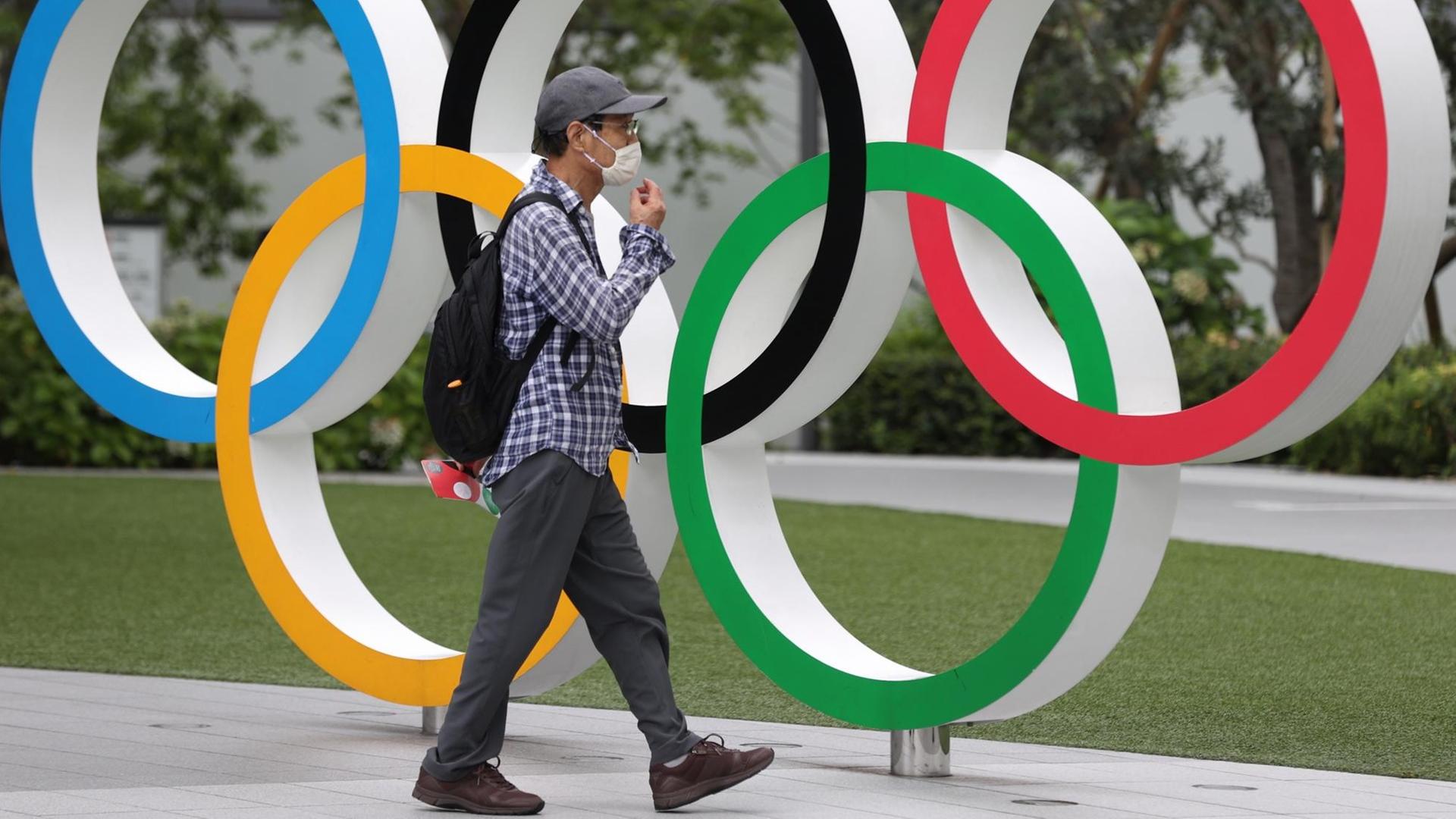 Ein Mann mit Maske läuft an einer Installation Olympischer Ringe vorbei, die in Tokio an die wegen Corona verschobene Sportveranstaltung erinnert.