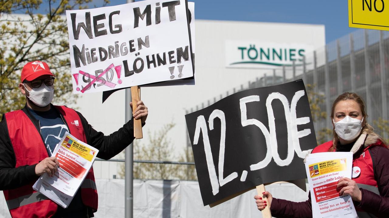 "Weg mit niedrigen Löhnen!" und "12,50 €" steht auf Plakaten, die ein Gewerkschaftsvertreter und eine Gewerkschaftsvertreterin in der Hand halten. Mit der Aktion wird vor dem Werk von Tönnies für höhere Löhne protestiert.