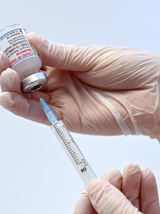 Eine Hand hält eine Impfdose mit dem Moderna mRnA-Impfstoff und zieht ihn mit einer Spritze heraus