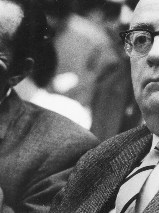 Adorno und Böll sitzen in einem Hörsaal und schauen nach vorn.