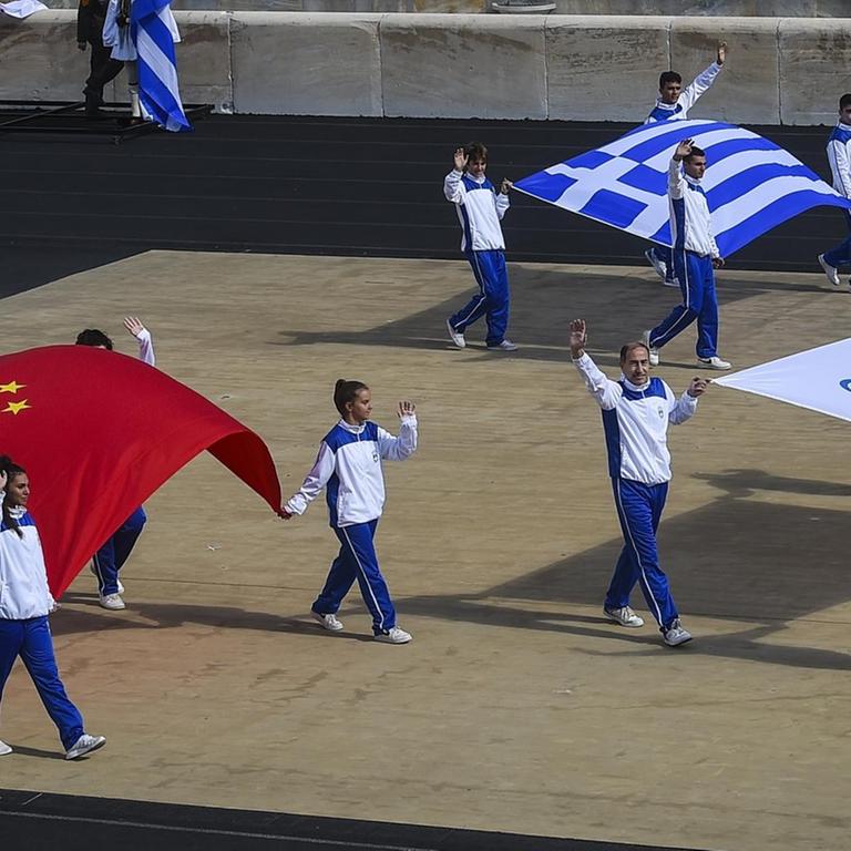 Delegationen tragen die Flaggen Chinas, (vorn l), Griechenlands, Chinas und die Olympische Flagge (r) während der Zeremonie zur Übergabe der Flamme für die Olympischen Winterspiele 2022 im Panathenäischen Stadion. Die Olympischen Winterspiele finden vom 4. bis 20. Februar 2022 in Peking statt.