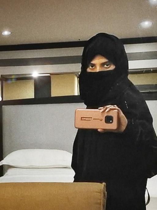 Filmstill aus "Saudi Runaway", eine schwarz verschleierte Frau macht ein Selfie von sich im Spiegel mit ihrem Telefon.