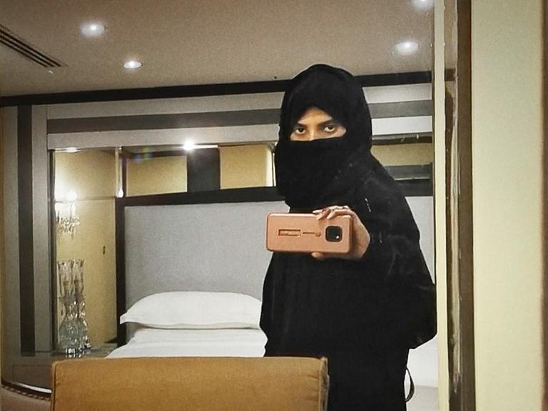 Filmstill aus "Saudi Runaway", eine schwarz verschleierte Frau macht ein Selfie von sich im Spiegel mit ihrem Telefon.