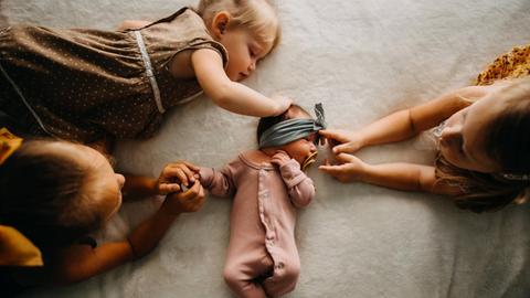 Drei Schwestern berühren ein kleines Baby in ihrer Mitte