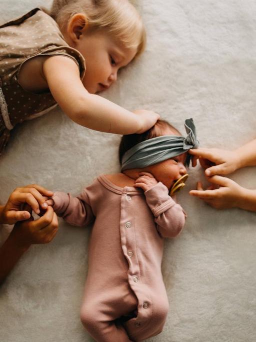 Drei Schwestern berühren ein kleines Baby in ihrer Mitte