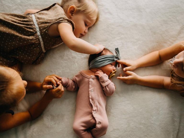 Drei Schwestern berühren ein kleines Baby in ihrer Mitte