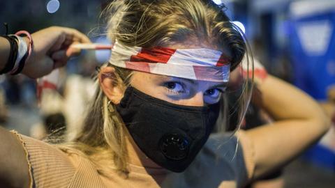 Demonstrantin in Budapest wickelt sich rot-weißes Flatterband um den Kopf.