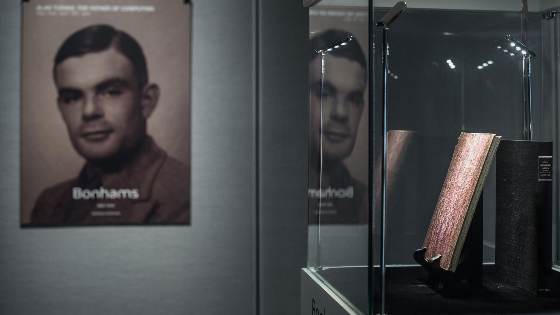 In einer Vitrine werden handschriftliche Notizen von Alan Turing (1912-1954) ausgestellt, im Hintergrund ein Plakat mit einem Foto des britischen Mathematikers.