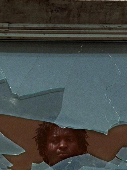 Ein Asylbewerber schaut am 23.9.1991 aus einem eingeschlagenen Fenster des Asylbewerberheims im sächsischen Hoyerswerda