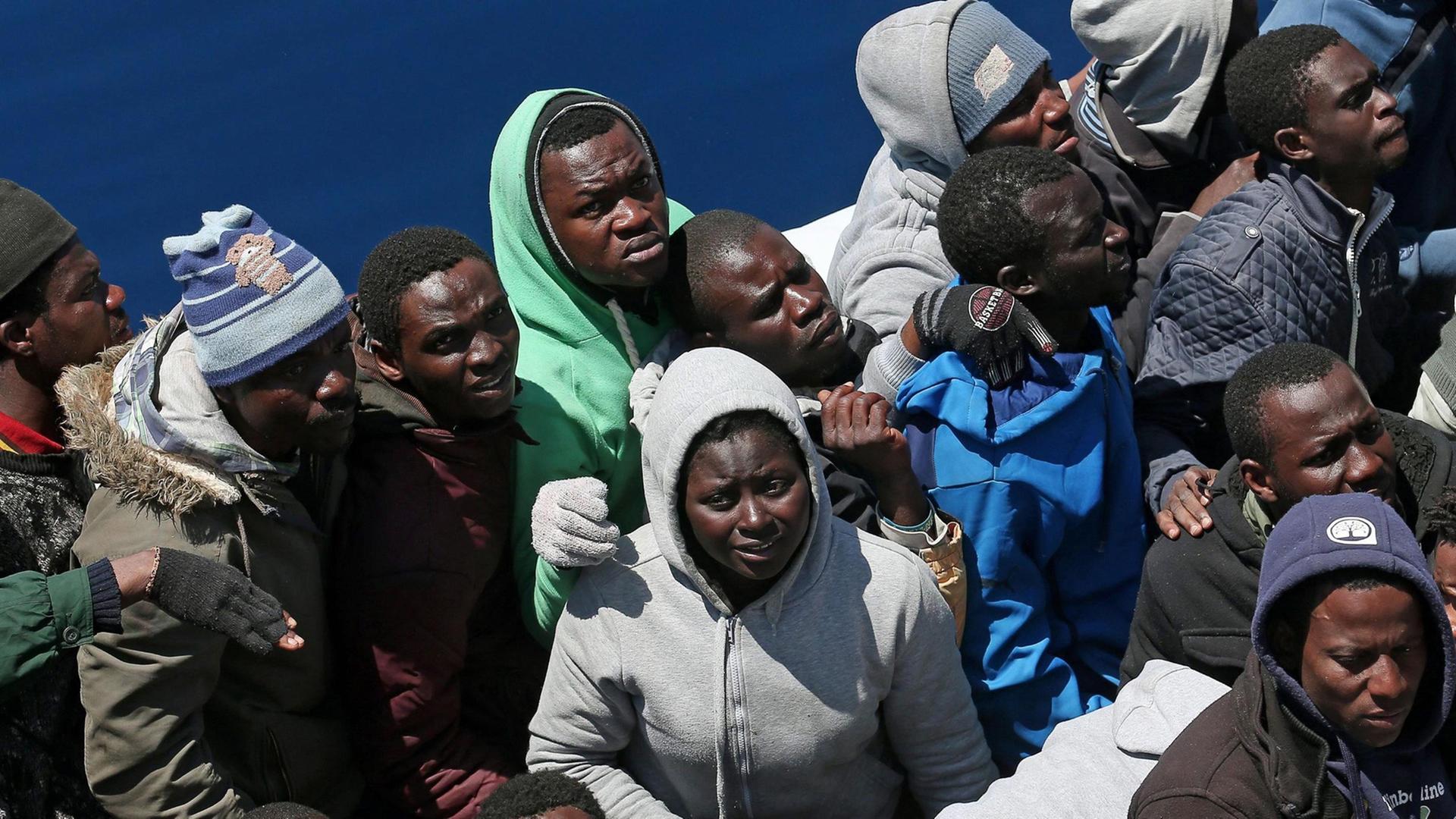 Ein Dutzend Flüchtlinge drängen sich auf einem kleinen Boot im Mittelmeer, bevor sie auf das Schiff der Küstenwache gelangen können.