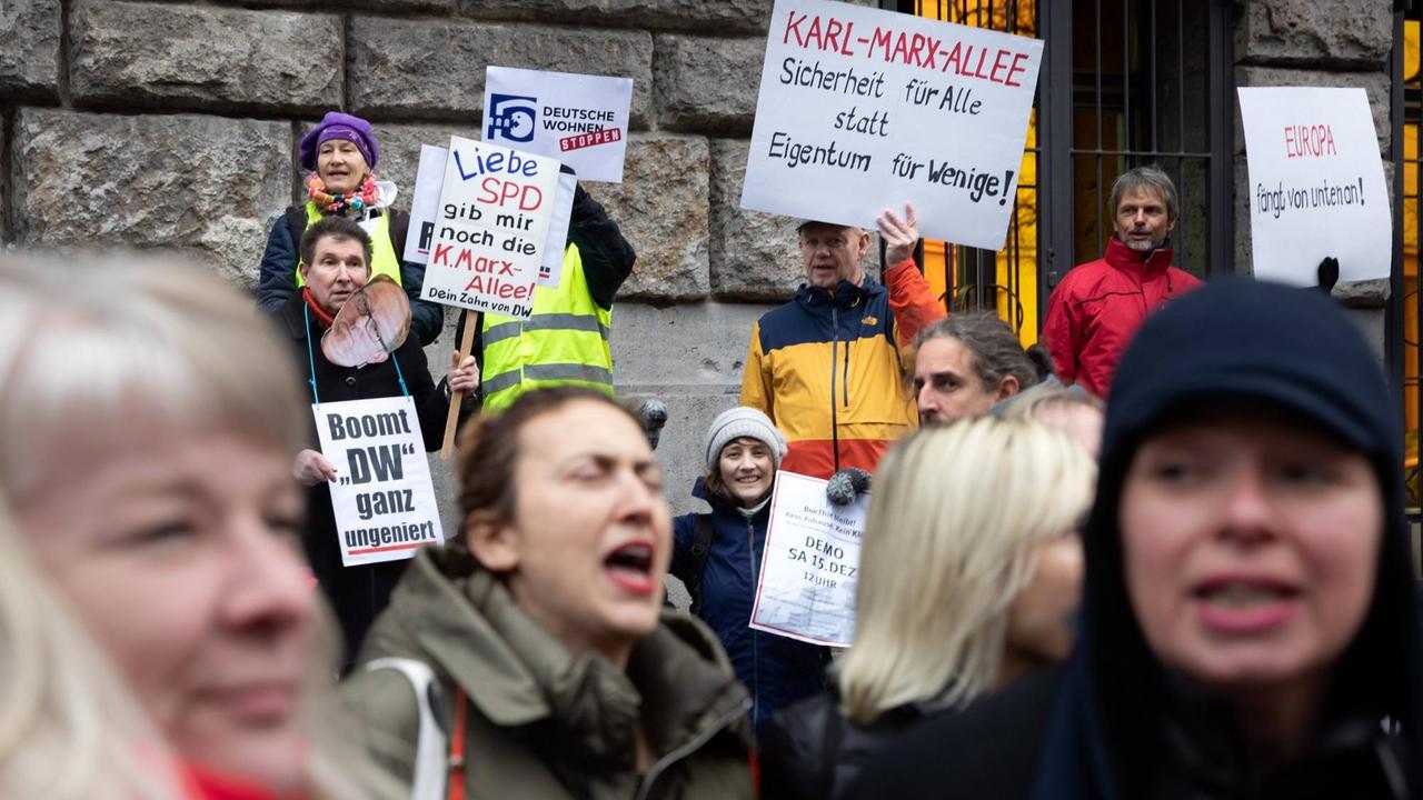Menschen rufen Parolen und halten Protest-Plakate gegen den Verkauf der Gebäude in der Berliner Karl-Marx-Allee hoch.