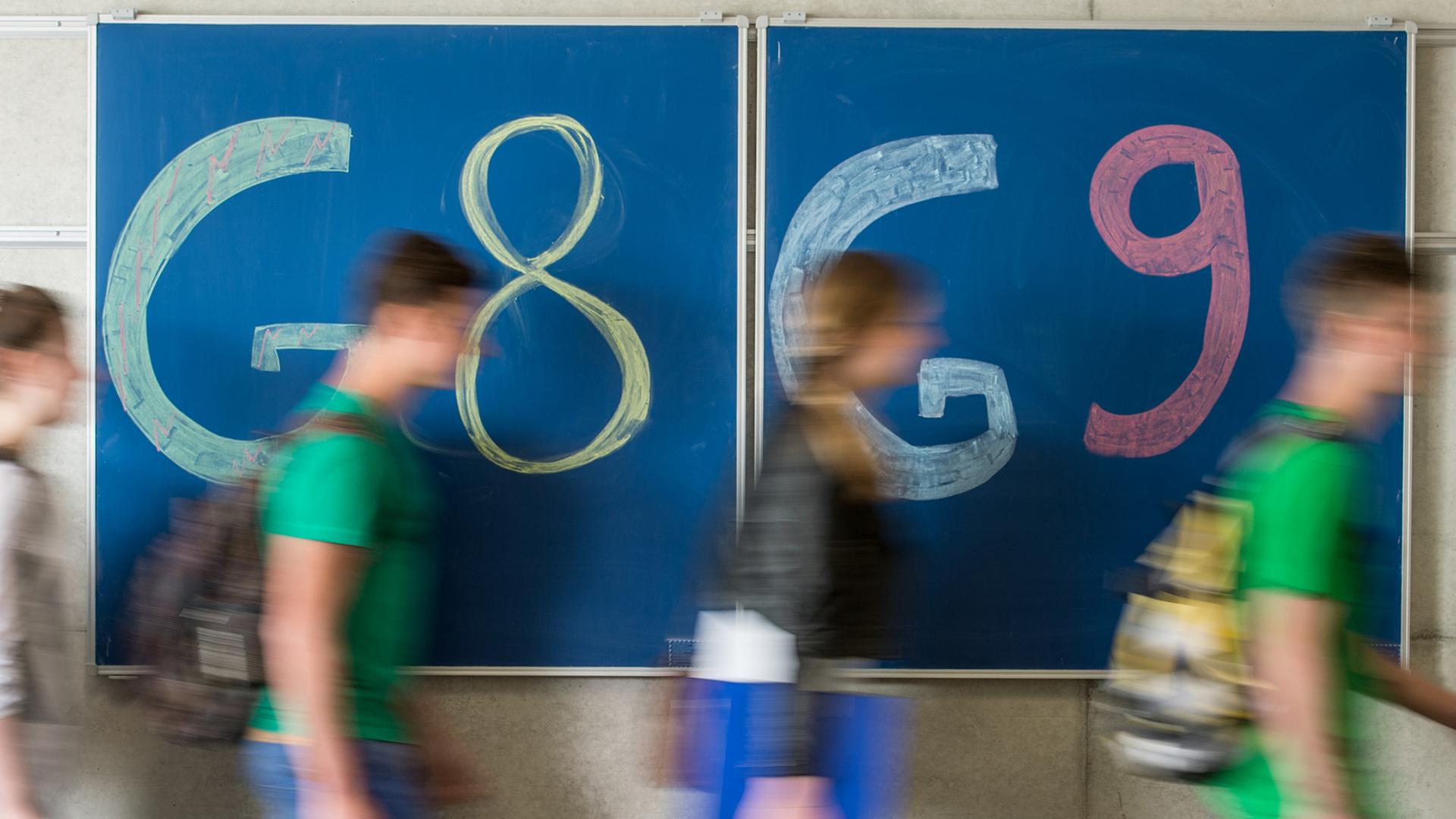 Schüler gehen an einer Tafel vorbei, auf der "G8" und "G9" steht.