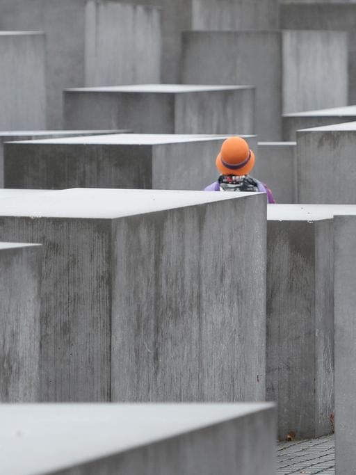 Eine Frau mit buntem Hut steht am 09.12.2013 in Berlin im Nieselregen zwischen den Stelen des Holocaust-Mahnmals in Berlin.