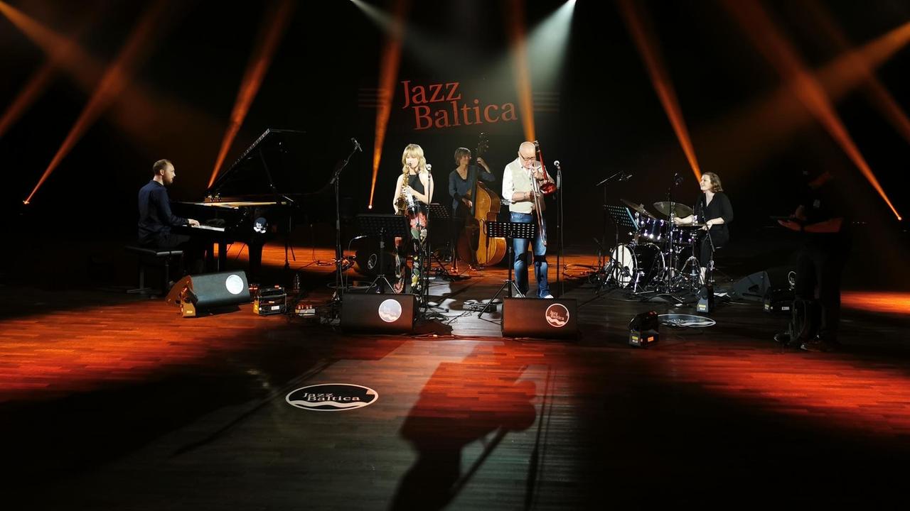 Fünf Musikerinnen und Musiker spielen auf einer in rot ausgeleuchteten Bühne beim Festival Jazzbaltica