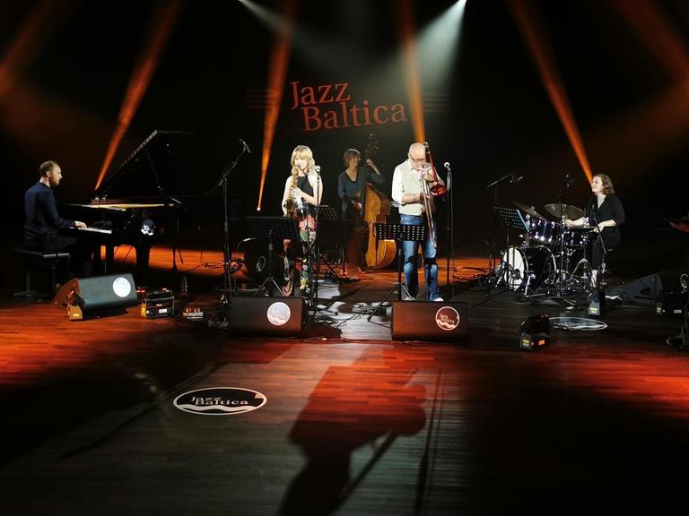 Fünf Musikerinnen und Musiker spielen auf einer in rot ausgeleuchteten Bühne beim Festival Jazzbaltica