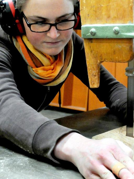 Eine Tischlerin schneidet ein Stück Holz zu.