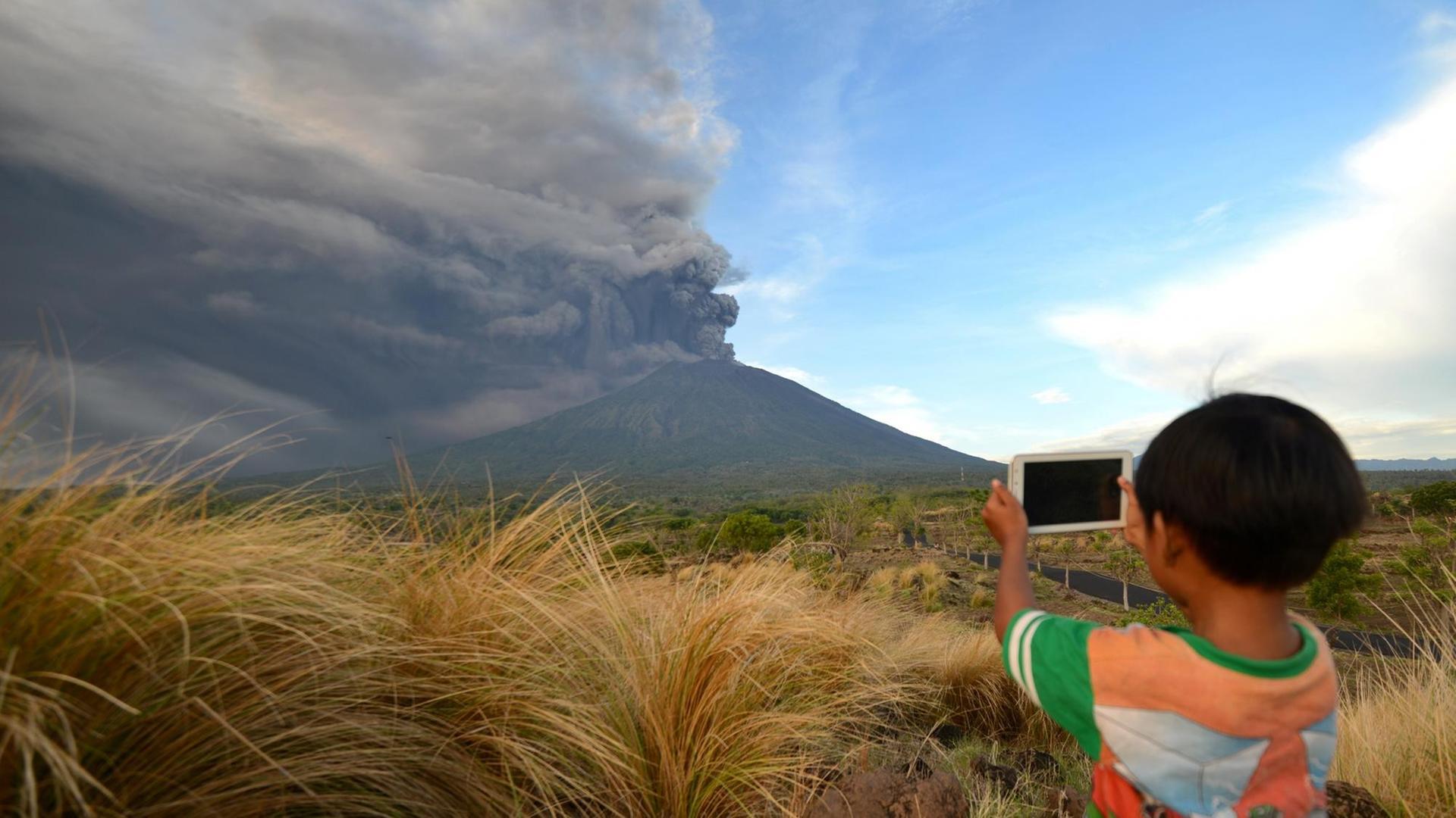 Ein kleiner Junge fotografiert vom Kubu sub-Distrikt in der Region Karangasem aus den erneut aktiven Vulkan Mount Agung auf der indonesischen Insel Bali am 26.11.2017./