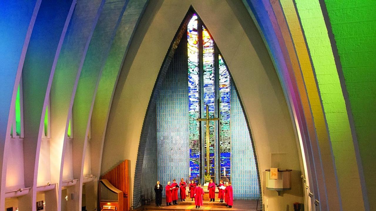 Ein einer bunt beleuchteten Kirche steht das Ensemble im Halbkreis im Altarraum.