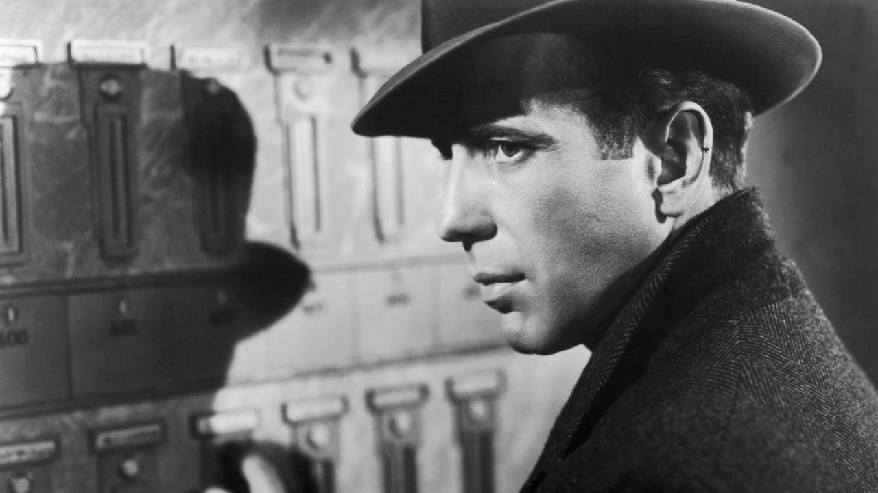 Der Schauspieler Humphrey Bogart im Profil, mit Hut, schwarz-weiß. Sein Hut wirft einen Schatten an die Wand.