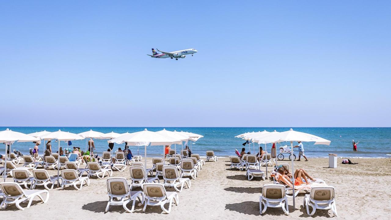 Ein Flugzeug beim Landeanflug über Touristen mit Sonnenliegen und Sonnenschirmen am Mackenzie Beach an einem heissen Sommertag, aufgenommen am 16. August 2018 in Larnaka, Zypern