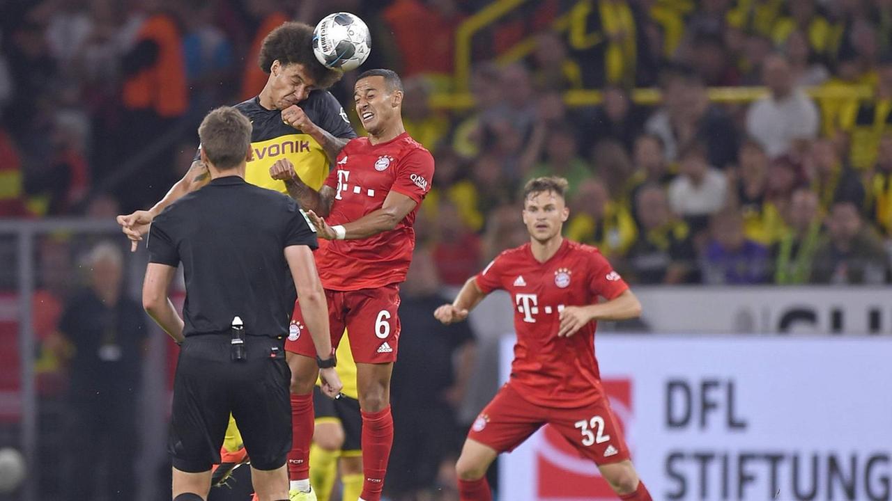 Spieler von Dortmund und München im Kampf um den Ball. Im Vordergrund steht der Schiedsrichter mit dem Rücken zur Kamera.