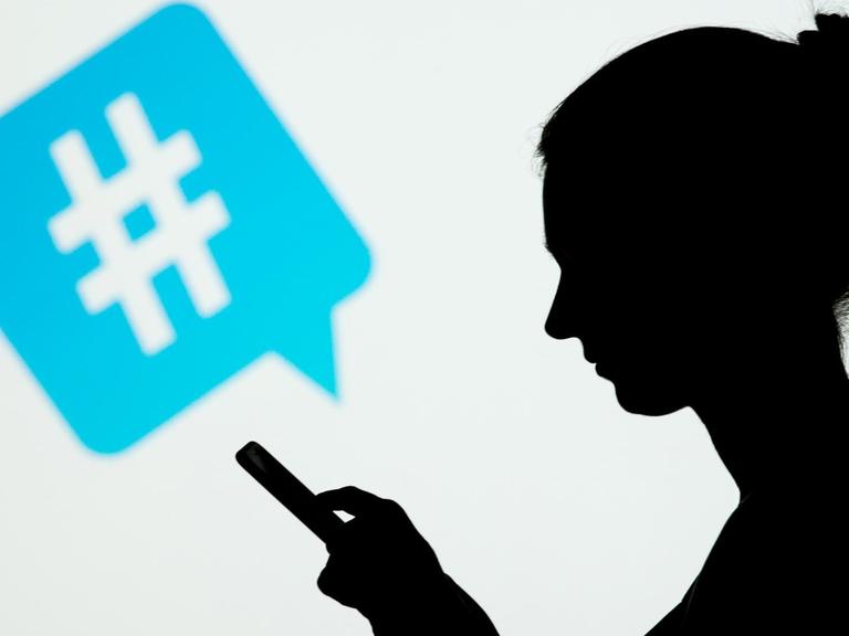 Die Silhouette einer Frau, die ein Smartphone in den Haenden haelt, ist am 08.01.2015 in Berlin vor dem Symbol eines Hashtags des sozialen Netzwerks Twitter zu sehen.