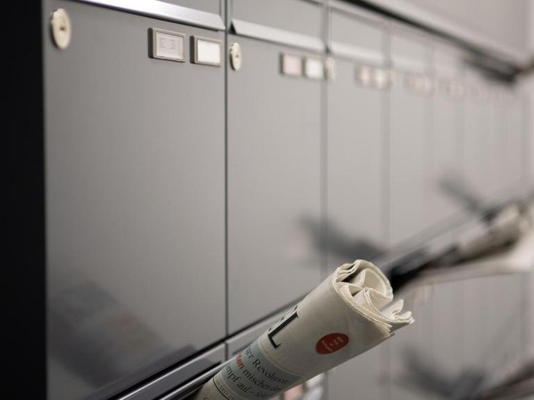 Mehrere Zeitungen stecken in Briefkästen im Flur eines Mehrfamilienhauses