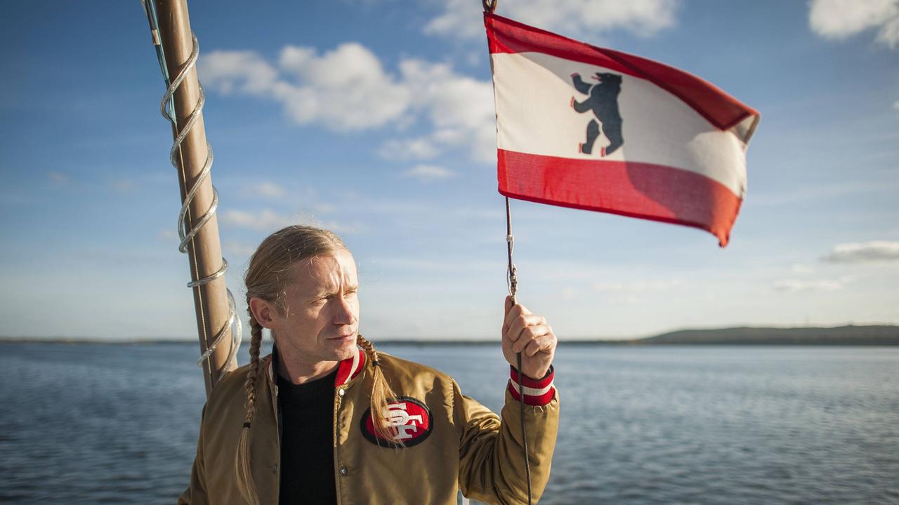 Der Rapper Romano auf einem Schiff, eine Berlin-Flagge in der Hand. 