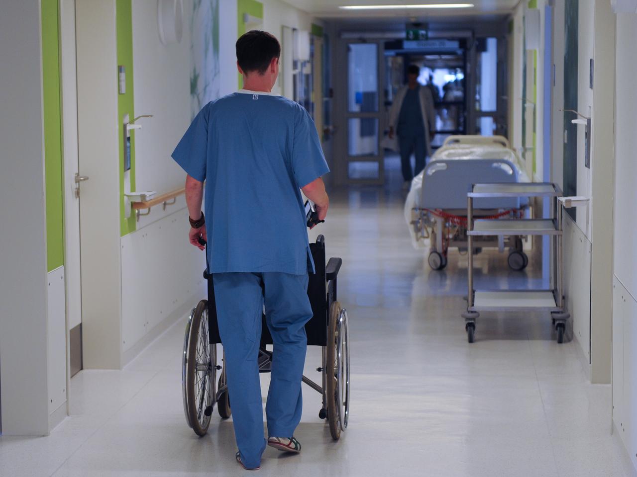Ein Pfleger schiebt einen Rollstuhl durch einen Krankenhausflur.